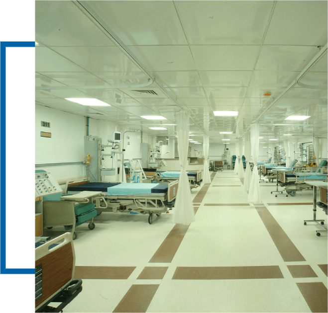 A clean, well-lit hospital ward with multiple empty beds, medical equipment, and partitions in place.